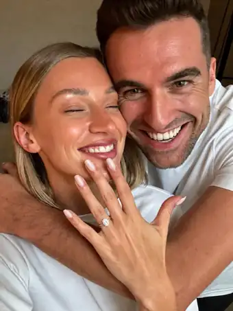 A smiling couple embracing, with the ring on her hand clearly visible.