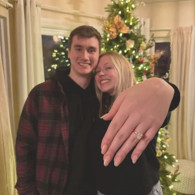 A Velur customer couple shows off their engagement ring in front of a Christmas tree