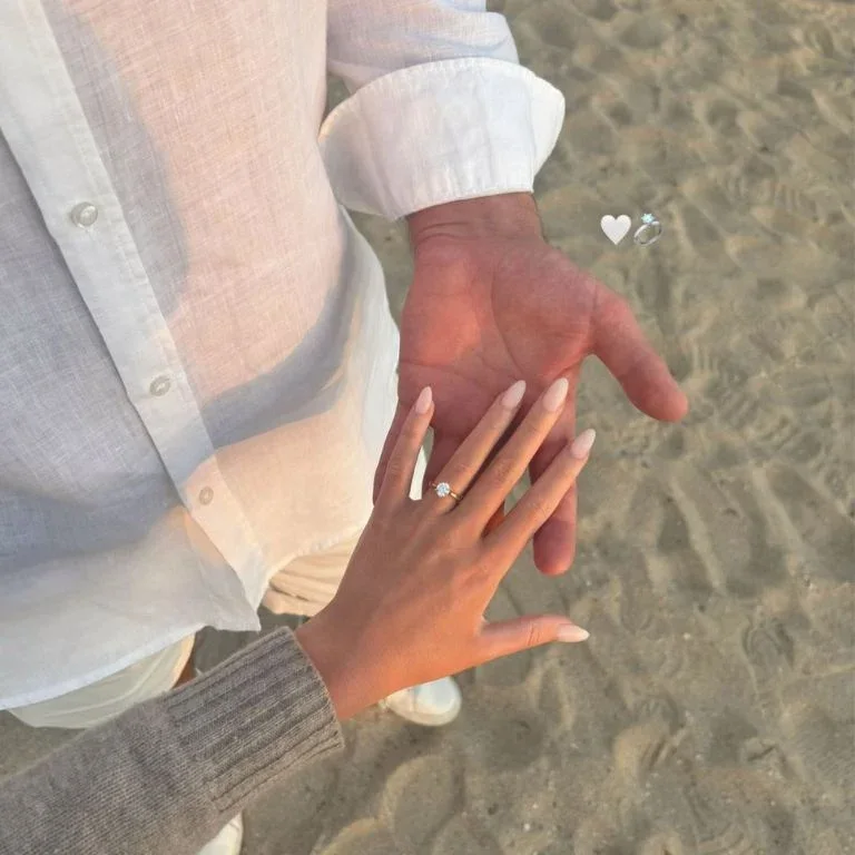 An engagement ring on a couple's hand on the beach