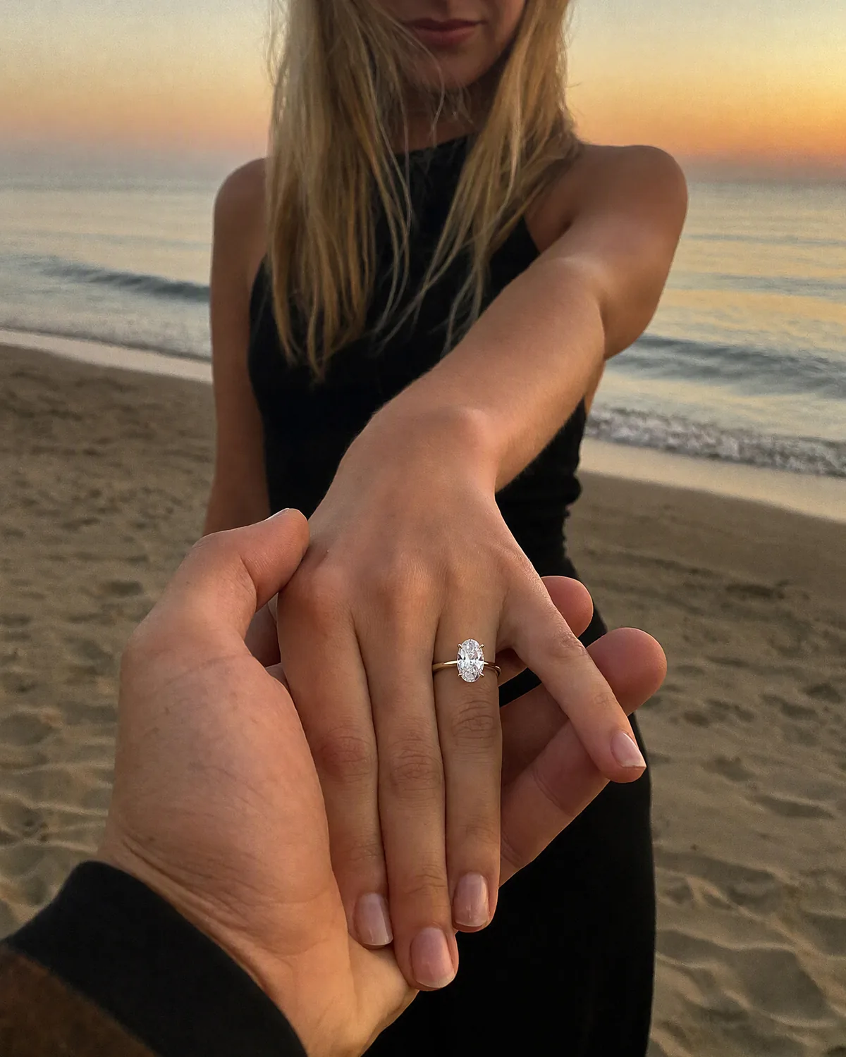 Verlobungsring an zwei Händen bei Sonnenuntergang am Strand