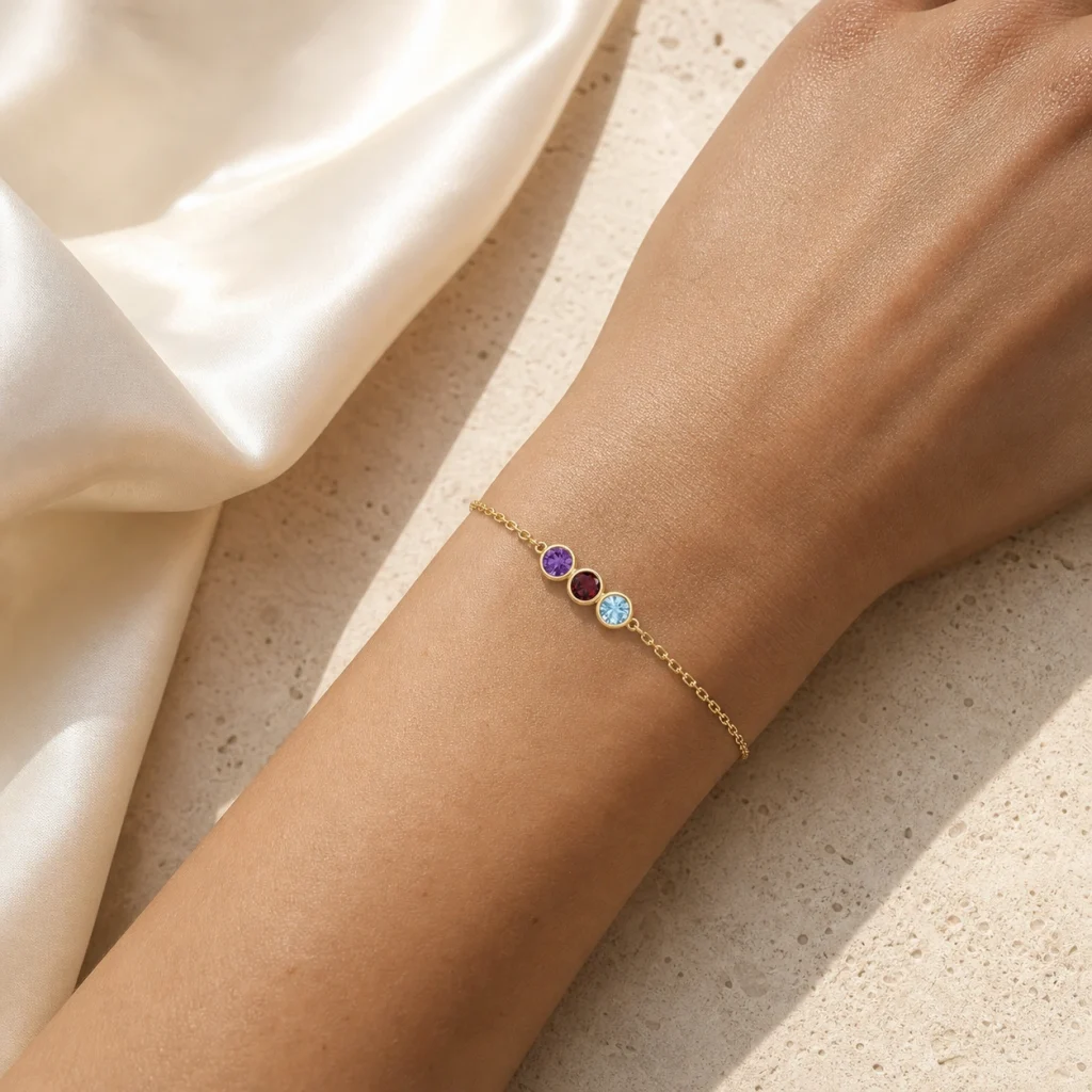 Liora Trio Geburtsstein-Armband mit Amethyst, Granat und Aquamarin am Handgelenk auf heller Seide