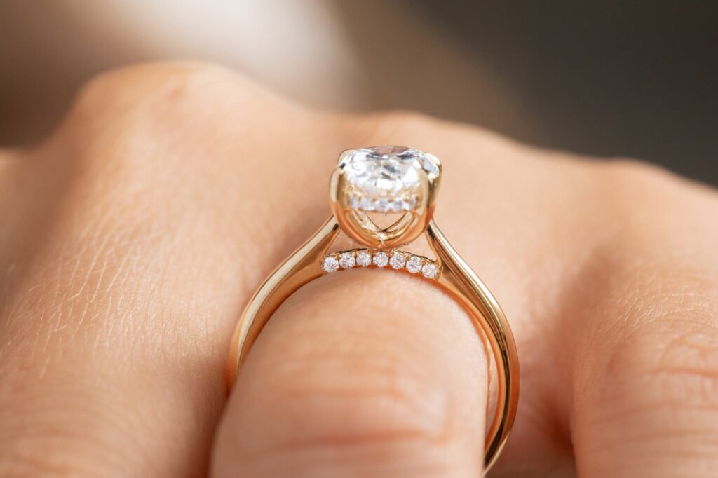 Verlobungsring in Gelbgold mit hoher Korbfassung, Hidden Halo und Pavé-Bridge am Finger