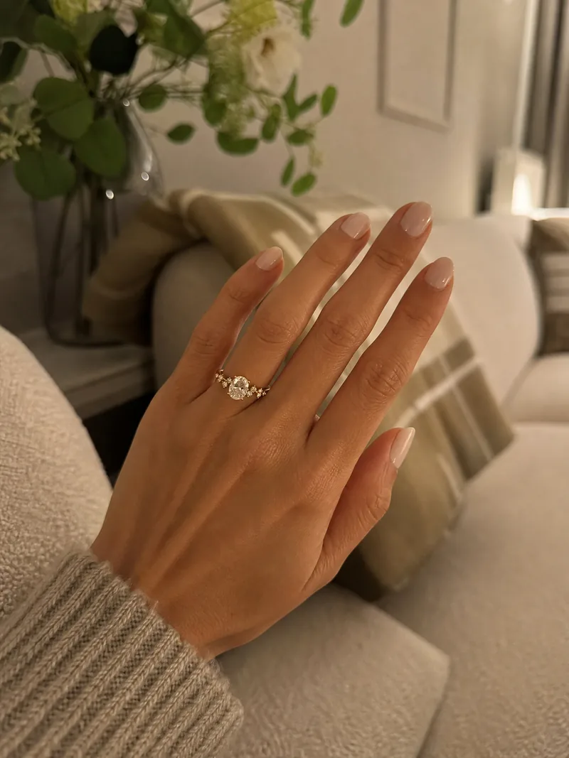 Floral Oval Verlobungsring an der Hand in einem hellen Zuhause.