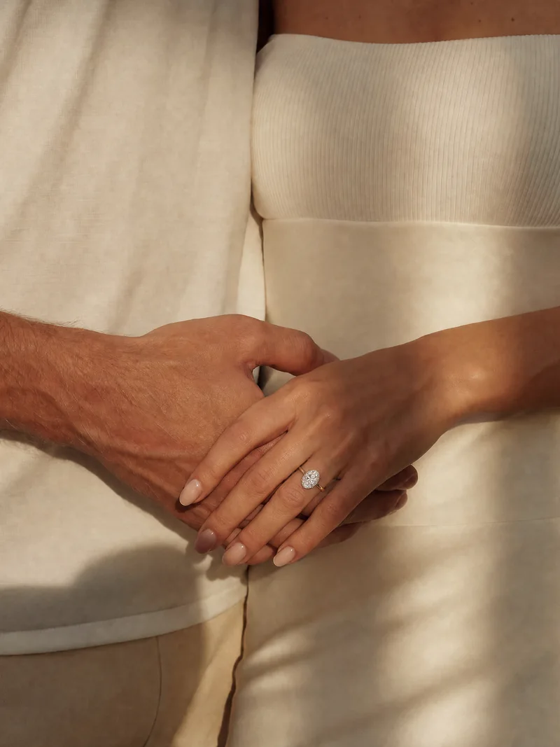 Hände eines Paares vor einem hellen Kleid, mit Ring am Finger.