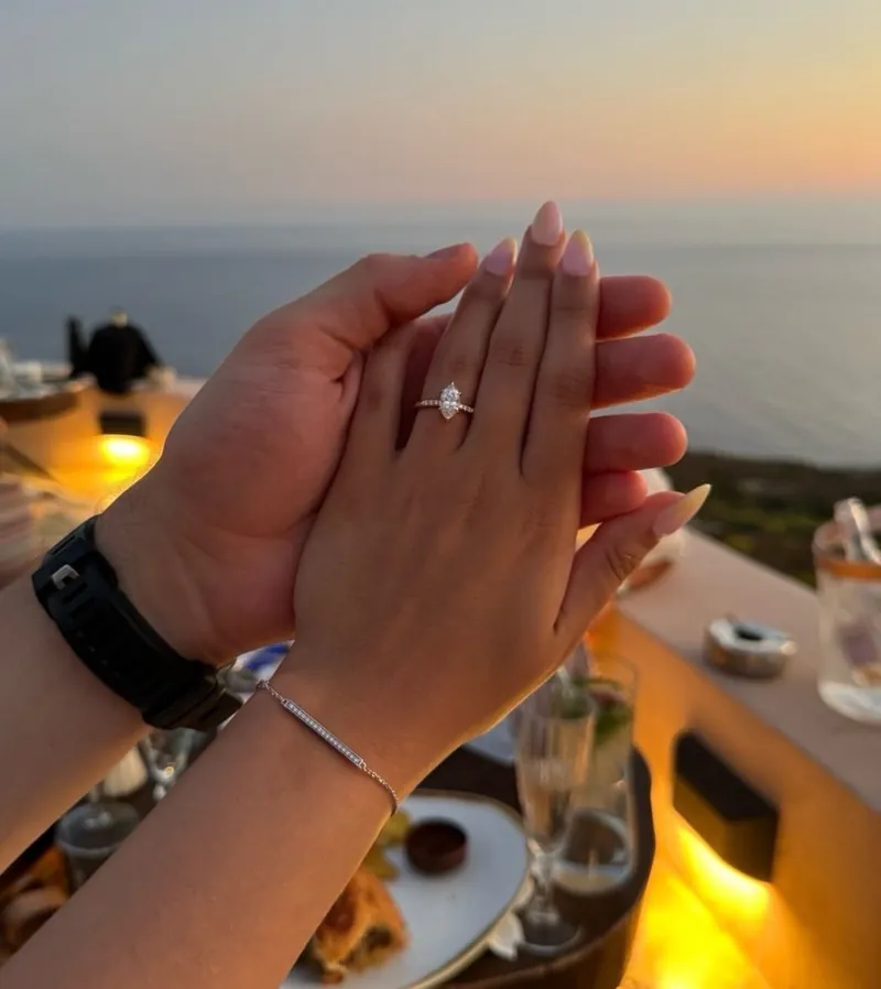 Zwei Hände im Sonnenuntergang am Meer, an ihrem Finger der Verlobungsring.