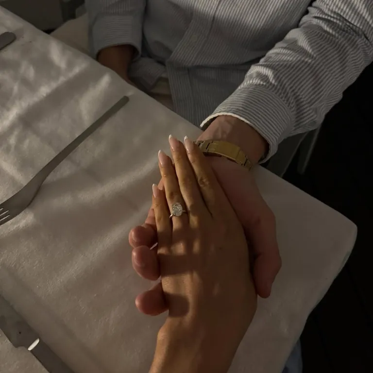 Hand in Hand am Tisch, an ihrem Finger der Verlobungsring.