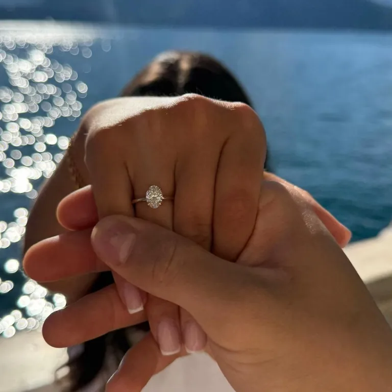 Ihre Hand mit Verlobungsring in seiner, dahinter glitzert das Meer.